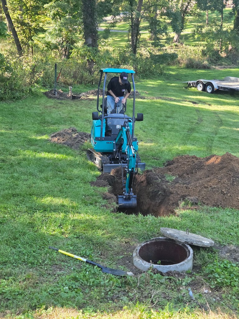 Doctor Rooter 911 mini excavator digging to reach a sewer line next to an open manhole