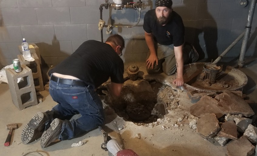 Technicians working on sewer and drainage excavation in a basement.