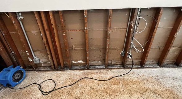 Water damage restoration in progress, showing exposed wall studs and a professional drying fan.